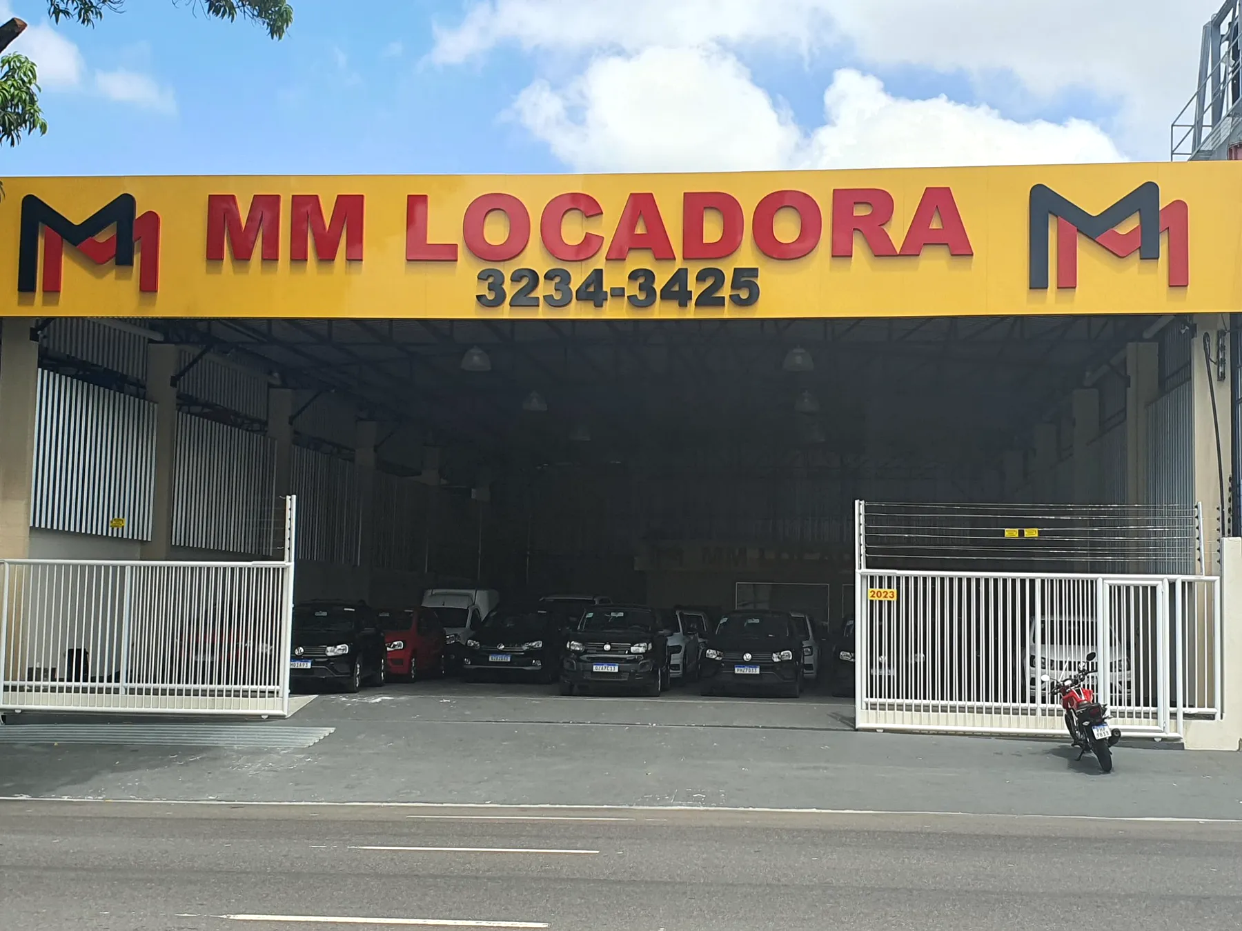 Fachada da MM Locadora com letreiro amarelo e galpão coberto para a frota.