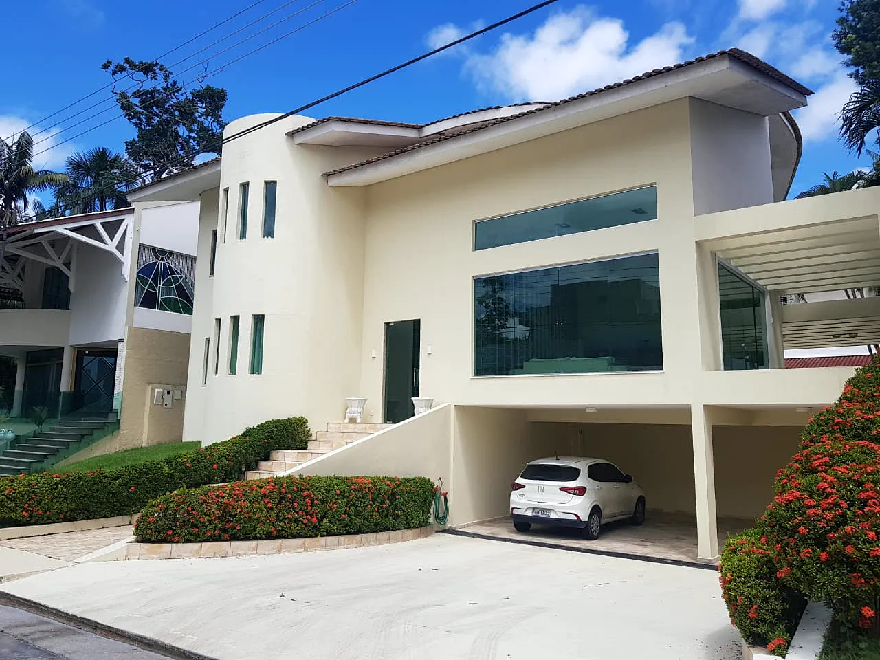 Fachada de residência clara com volume curvo, janelas verticais e garagem coberta.